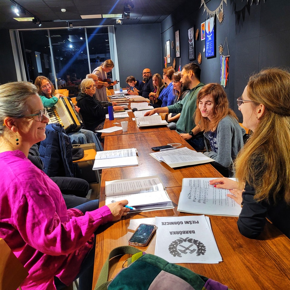 ludzie przy drewnianym długim stole ze śpiewnikami przed sobą